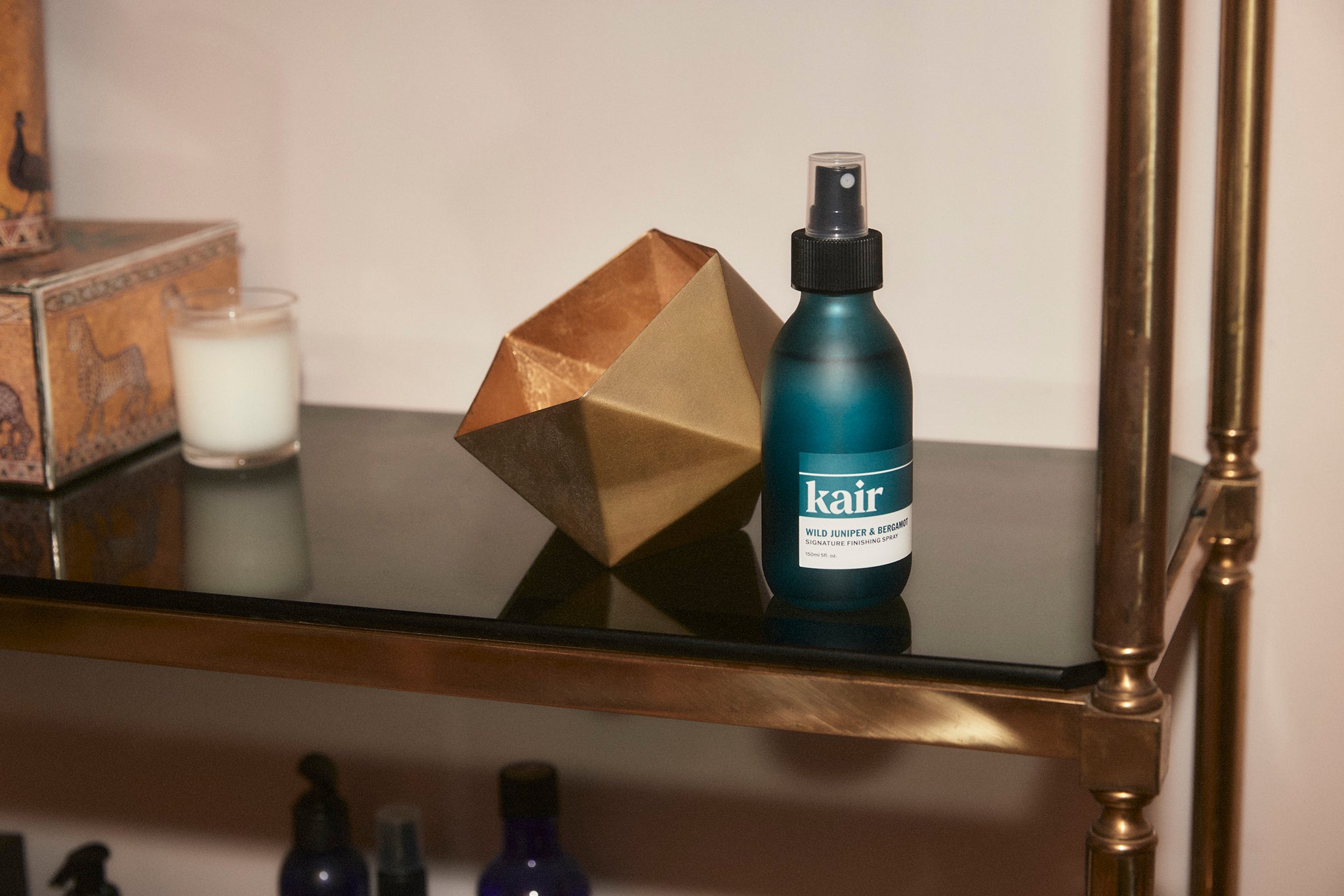 Kair Signature Finishing Spray in Wild Juniper & Bergamot, on a shelf next to a candle and gold ornament