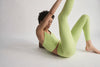 Woman wearing lime green activewear stretching in a white studio setting
