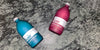 Photo of Kair Signature Fabric Conditioner bottles lying on a marble surface - one red (Cedarwood) and one blue (Wild Juniper)