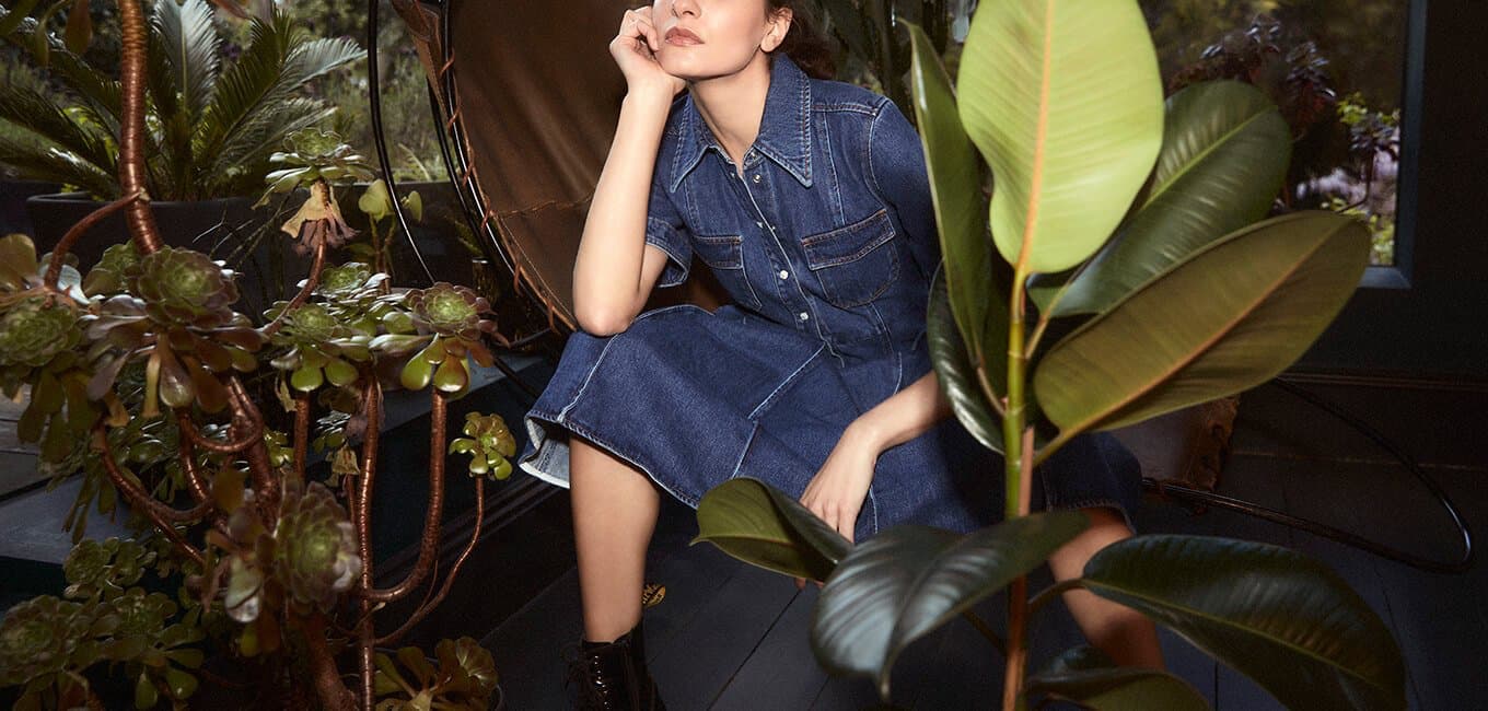 Woman wearing luxury denim sitting in a chair surrounded by plants