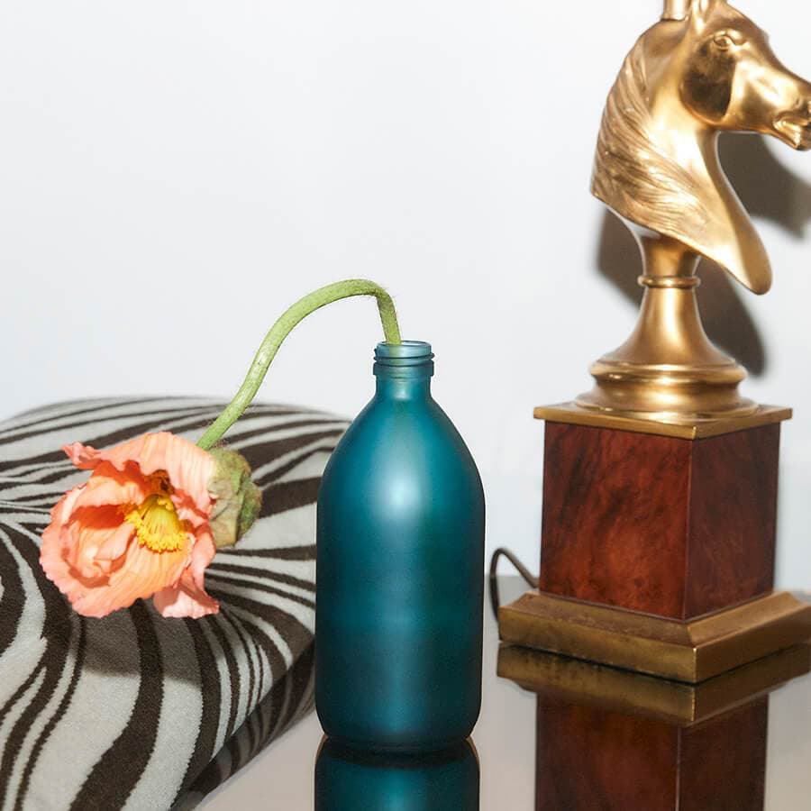 Kair Signature Clothing Wash - Wild Juniper & Bergamot bottle repurposed as a vase containing an orange flower