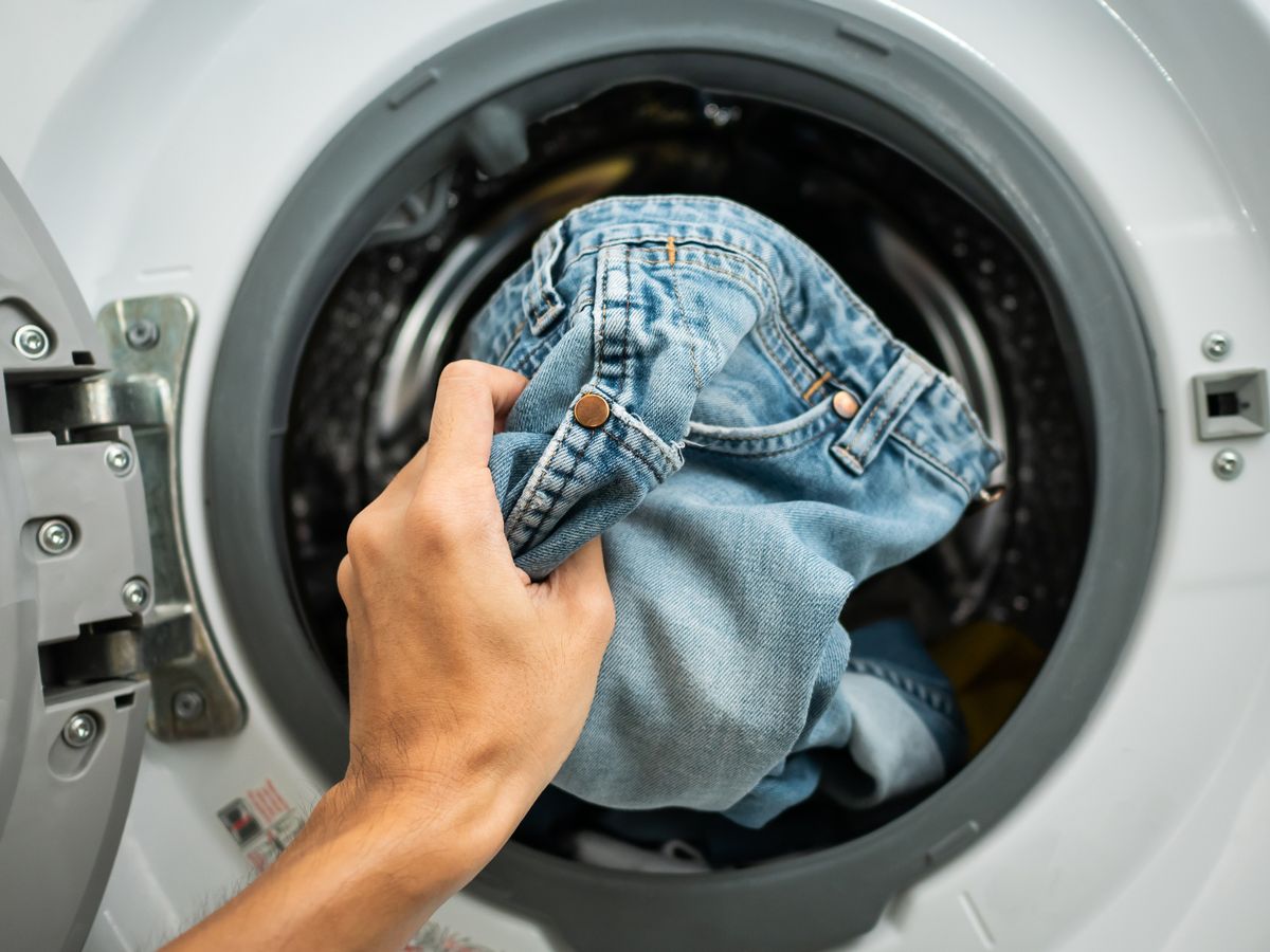 Photo of a hand putting a pair of blue jeans into a washing machine drum
