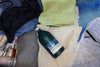 Kair Signature Wash bottle lying in a pile of clothes in a suitcase