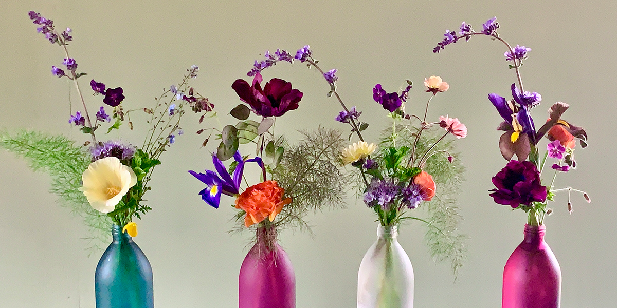 Four empty Kair bottles filled with beautiful flowers against a grey background