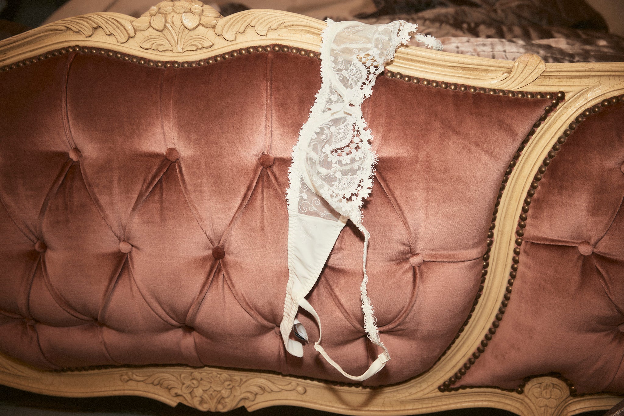 A white bra draped over a plush velvet sofa
