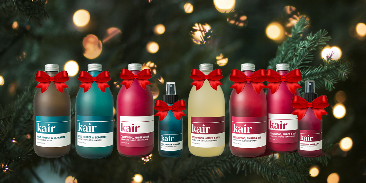 Kair bottles with a red bow on each bottle neck in a row against a background close-up image of a Christmas tree and lights