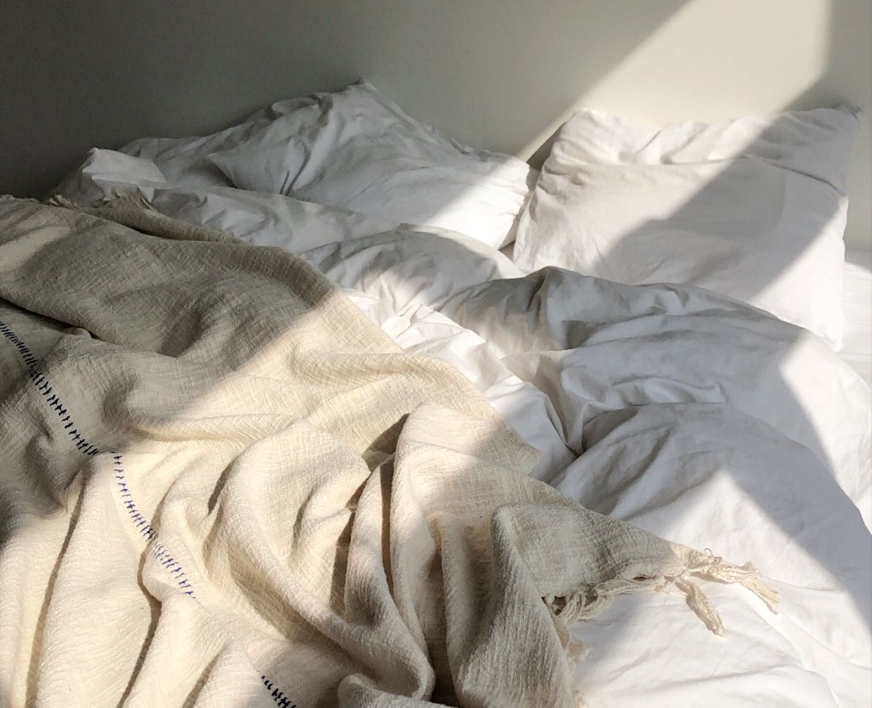 A bed with white cotton sheets and a natural linen throw