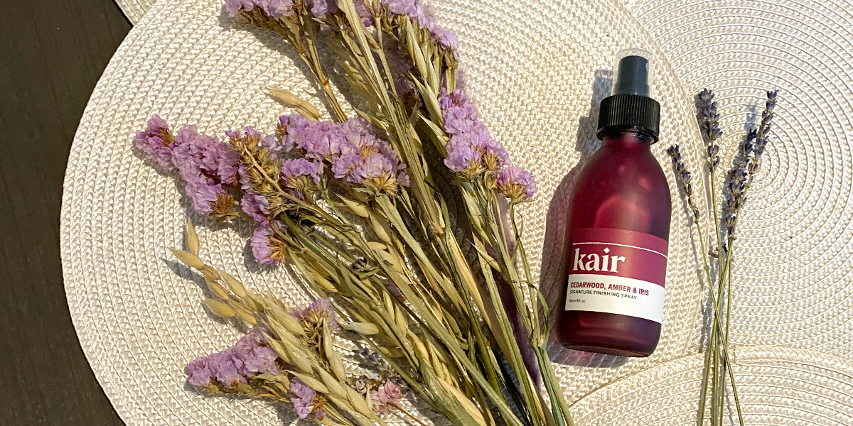 Kair's Signature Finishing Spray laying flat alongside dried purple flowers and lavender