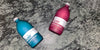 Photo of Kair Signature Fabric Conditioner bottles lying on a marble surface - one red (Cedarwood) and one blue (Wild Juniper) 