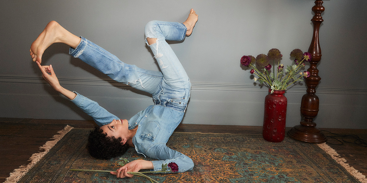 Woman wearing a denim jacket and jeans lying down and lifting one foot next to a vase of flowers
