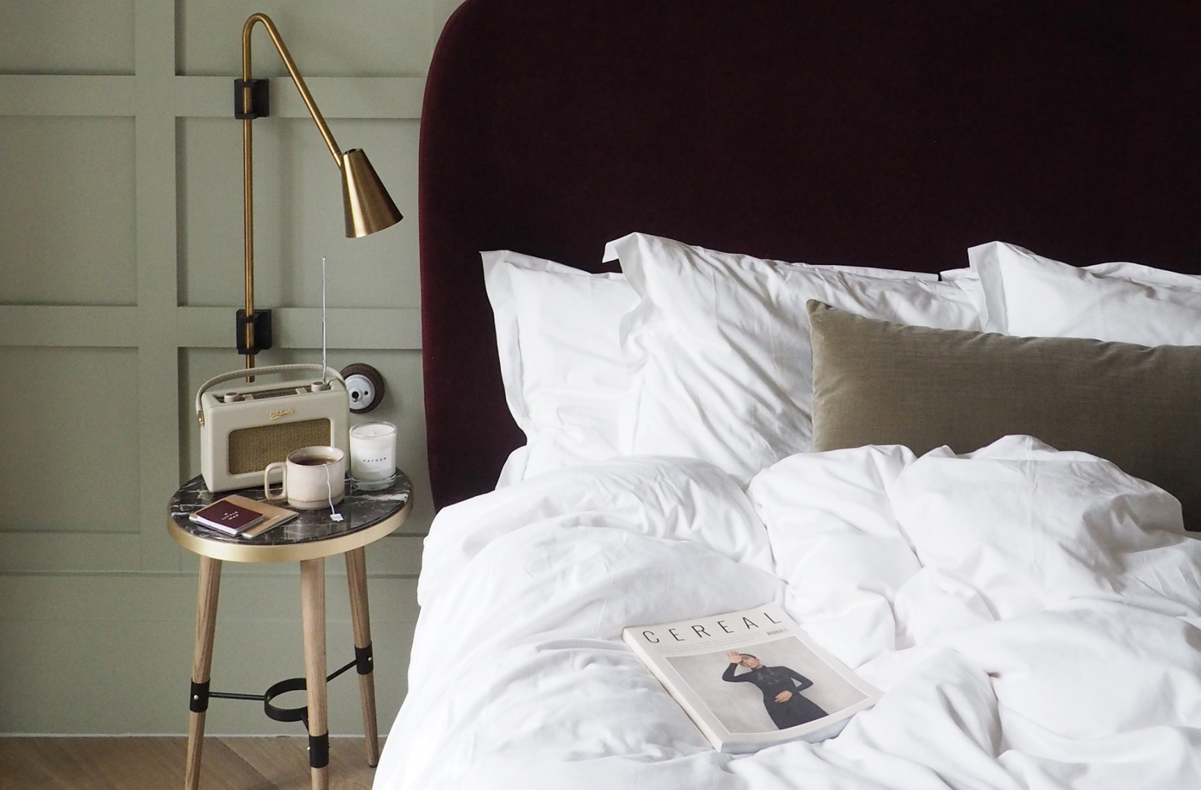 A bed with white sheets and a brass and marble side-table with a retro radio and a cup of tea