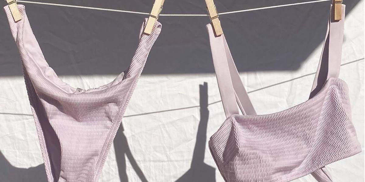 Lilac Bikini bottoms and bikini top handing on washing line with pegs. White sheet behind acting as background.