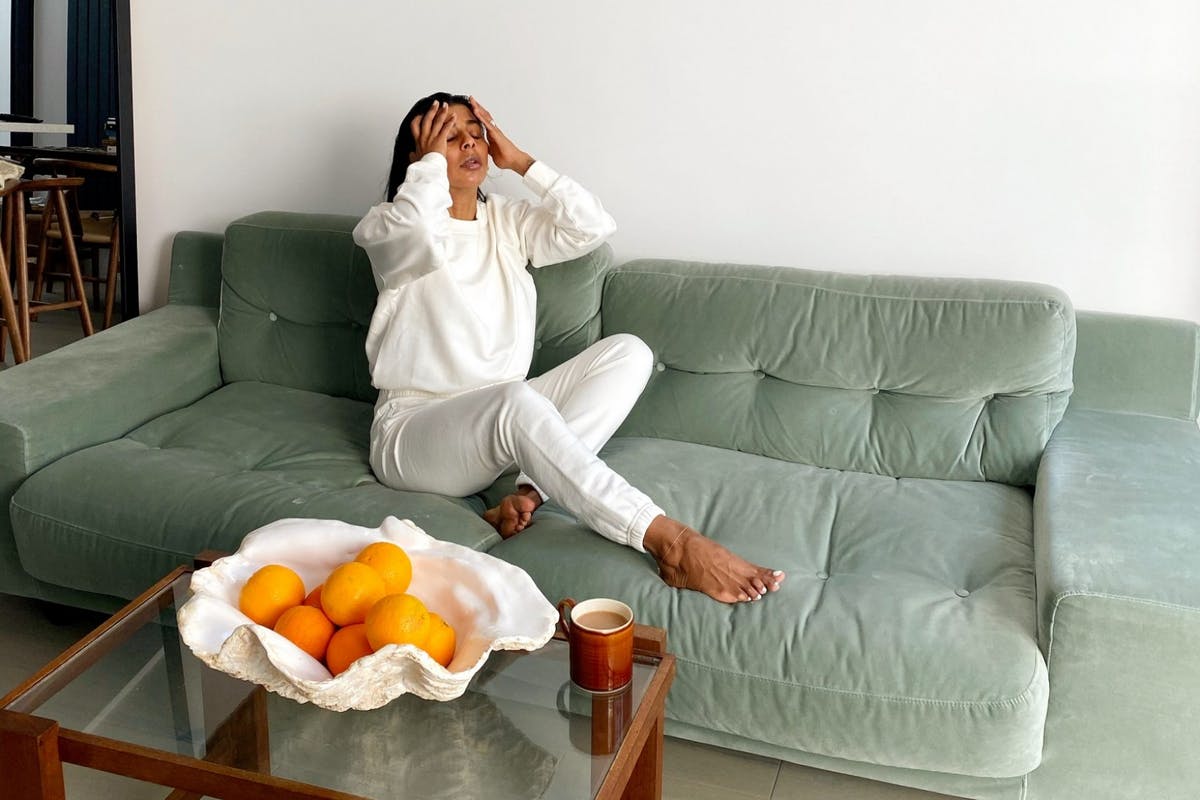 Photo showing Monikh sitting on a sage green sofa with a glass coffee table in front where a fruit bowl of oranges and a coffee cup are placed