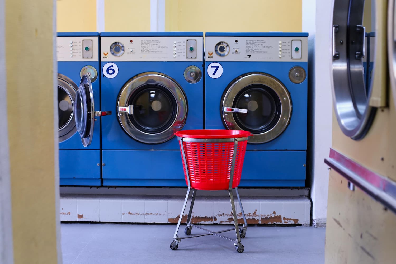 Three retro blue washing machines with a red laundry basket in front