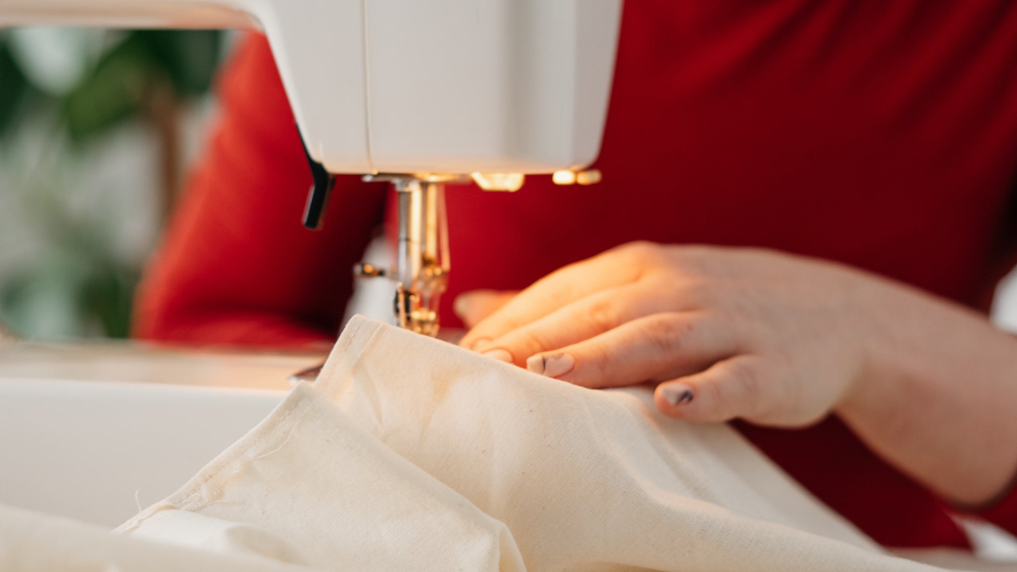 Photo of a woman wearing a red top using a white sewing machine to sew the edge of a cream fabric