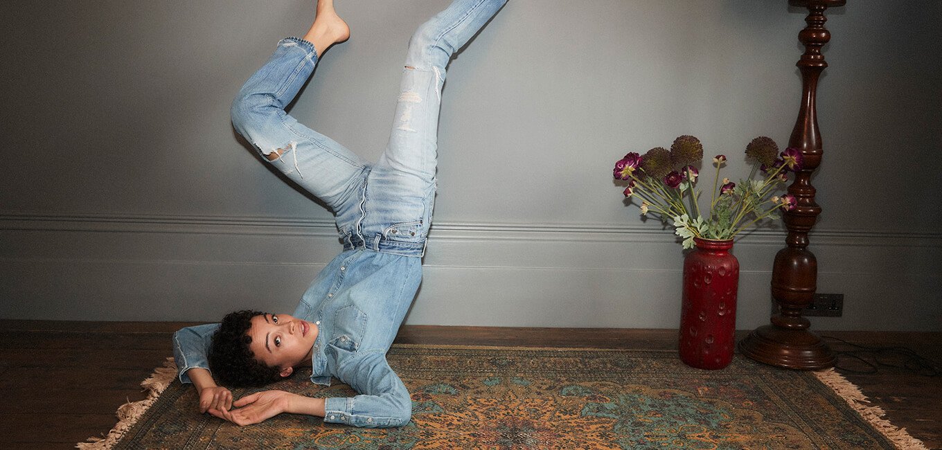 Model in denim clothing lying on a persian rug with legs against the wall